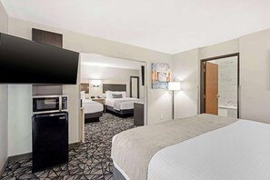 A hotel room with a bed, a flat-screen TV, a microwave, a refrigerator, and a bathroom visible through an open door.