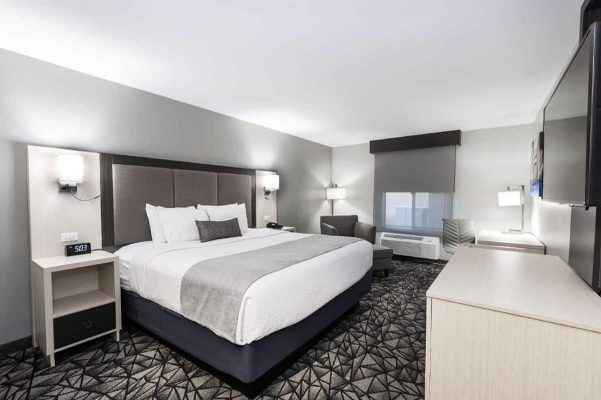 A hotel room with a bed, bedside tables, a desk, a chair, a TV, and a window.