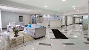 A modern hotel lobby with a grey sofa, armchairs, a coffee table, and a reception desk. - Best Western Morton Inn (Morton)