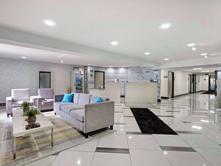 Un hall d’hôtel moderne avec un canapé gris, des fauteuils, une table basse et un comptoir d’accueil.