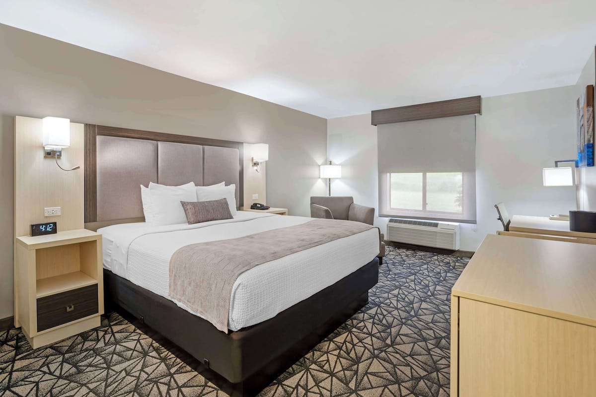 A hotel room with a large bed, bedside tables, a desk, and a window.