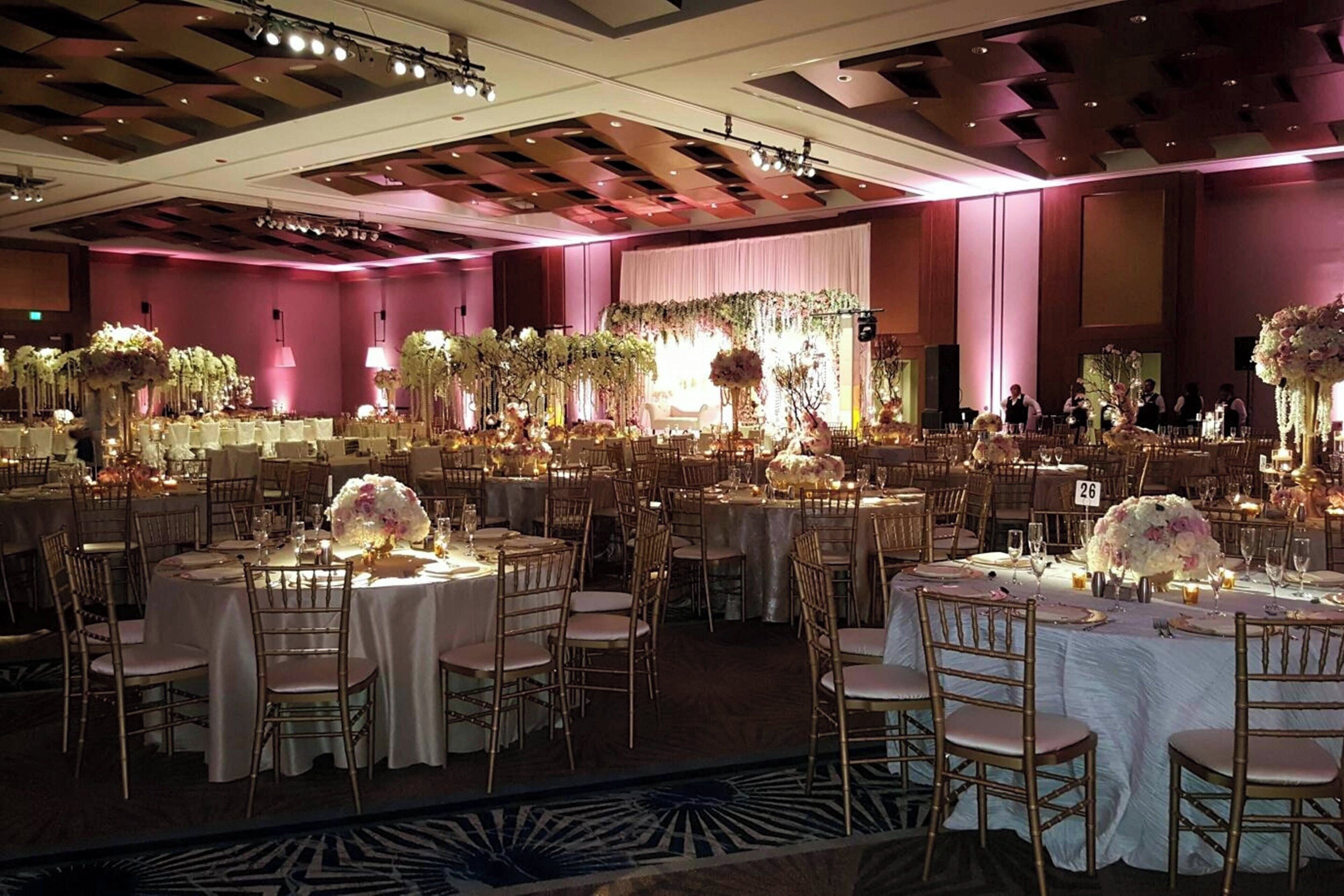 A banquet hall with round tables, gold chairs, and floral centerpieces.