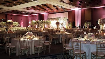 A banquet hall with round tables, gold chairs, and floral centerpieces.