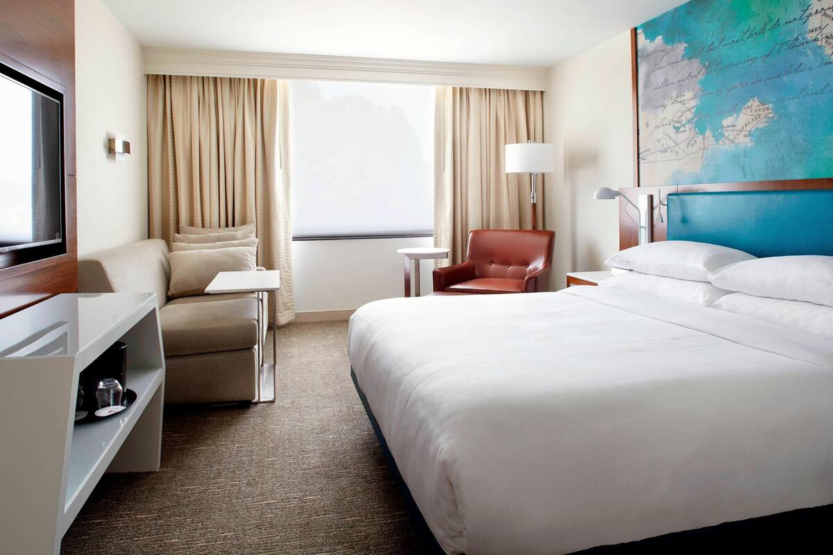 A hotel room with a large bed, a desk, a chair, a TV, and a map on the wall.