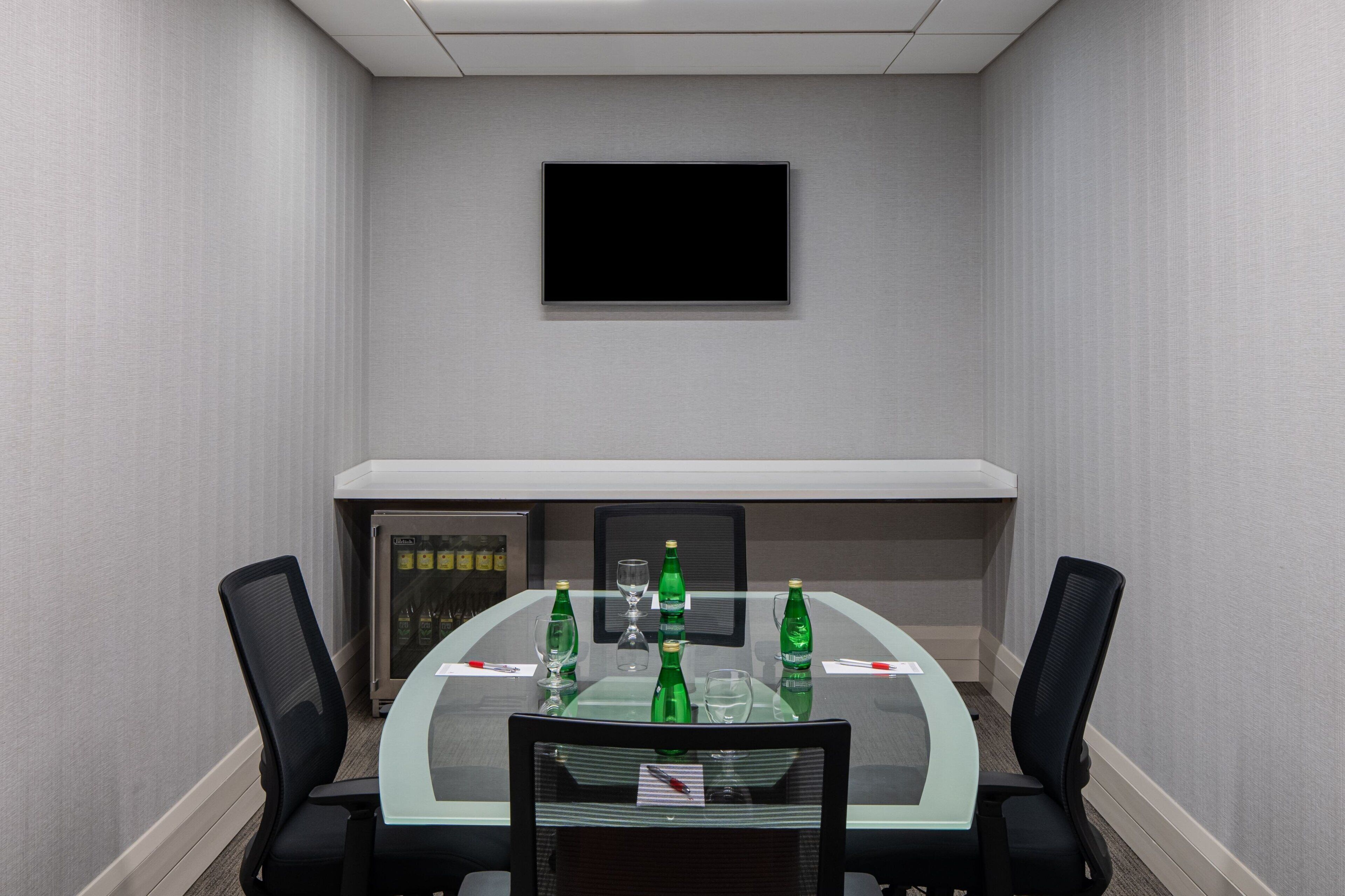 A conference room with a glass table, four chairs, a flat-screen TV, and a minibar.