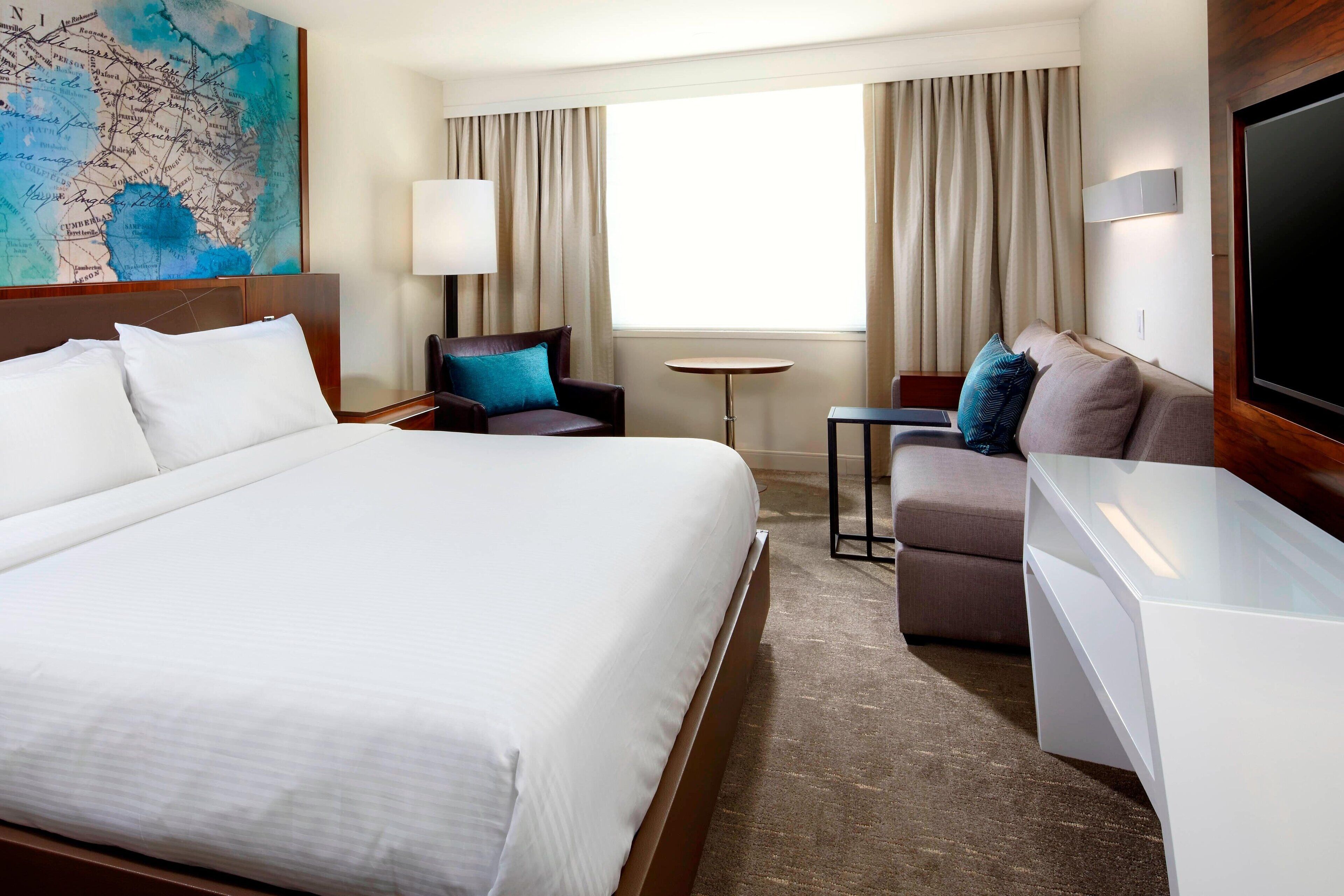 A hotel room with a large bed, a sofa, a small table, and a TV.