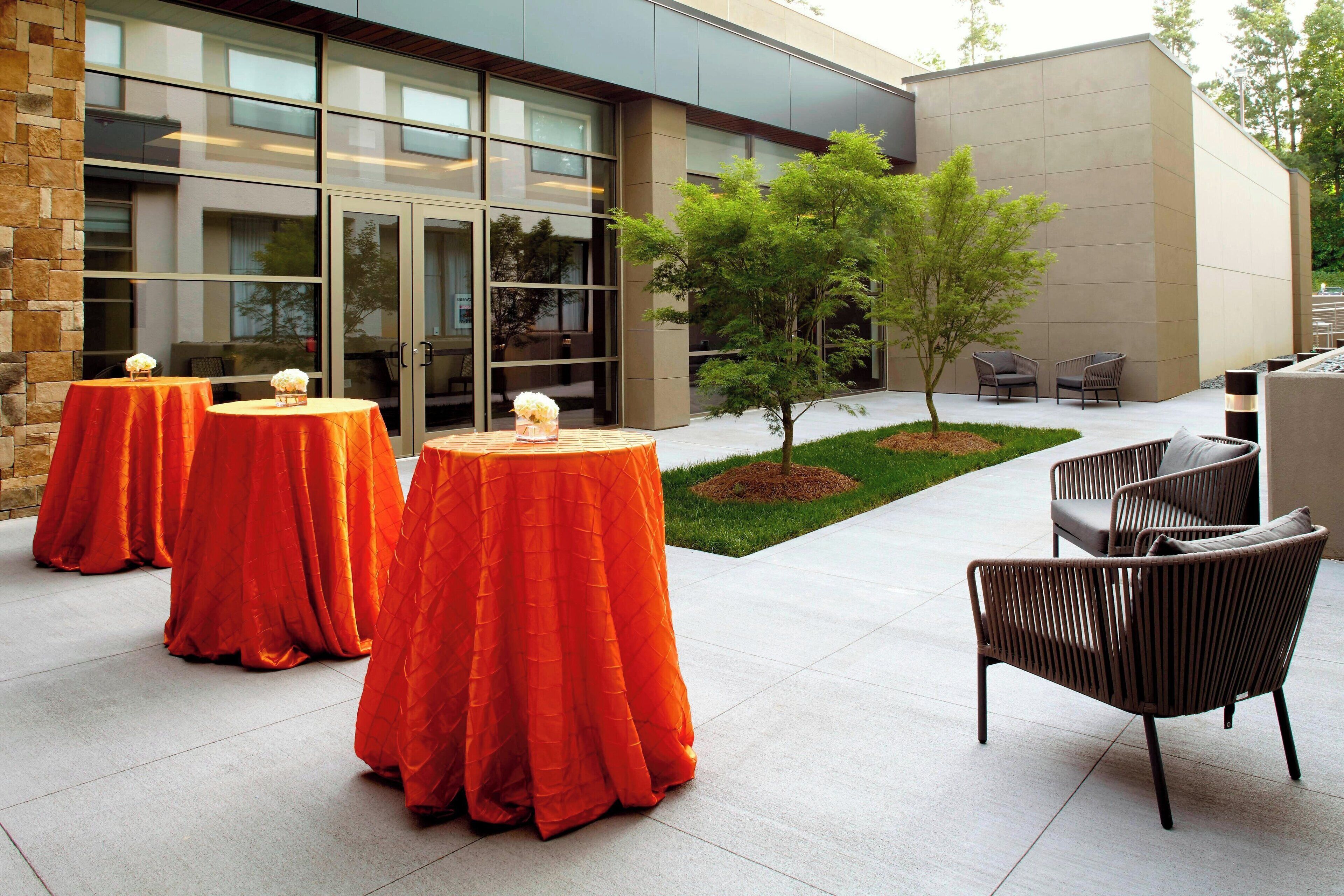 An outdoor patio area with three round tables covered with orange tablecloths, surrounded by wicker chairs.