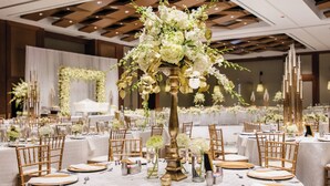 A banquet hall with round tables, gold chairs, and white tablecloths.
