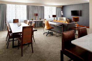 A hotel room with a dining area, a desk, two lamps, a TV, and a patterned wall.