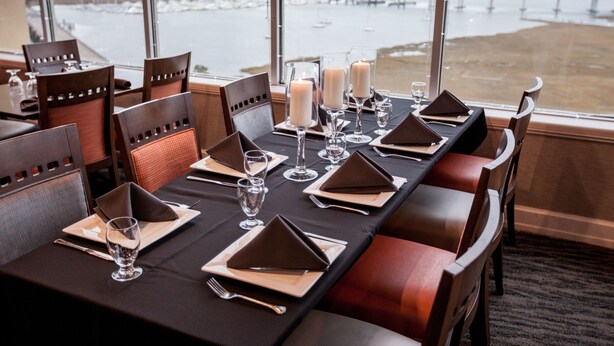A dining table set with place settings, glasses, and candles, overlooking a waterfront view. - Holiday Inn Charleston Riverview by IHG (Charleston)
