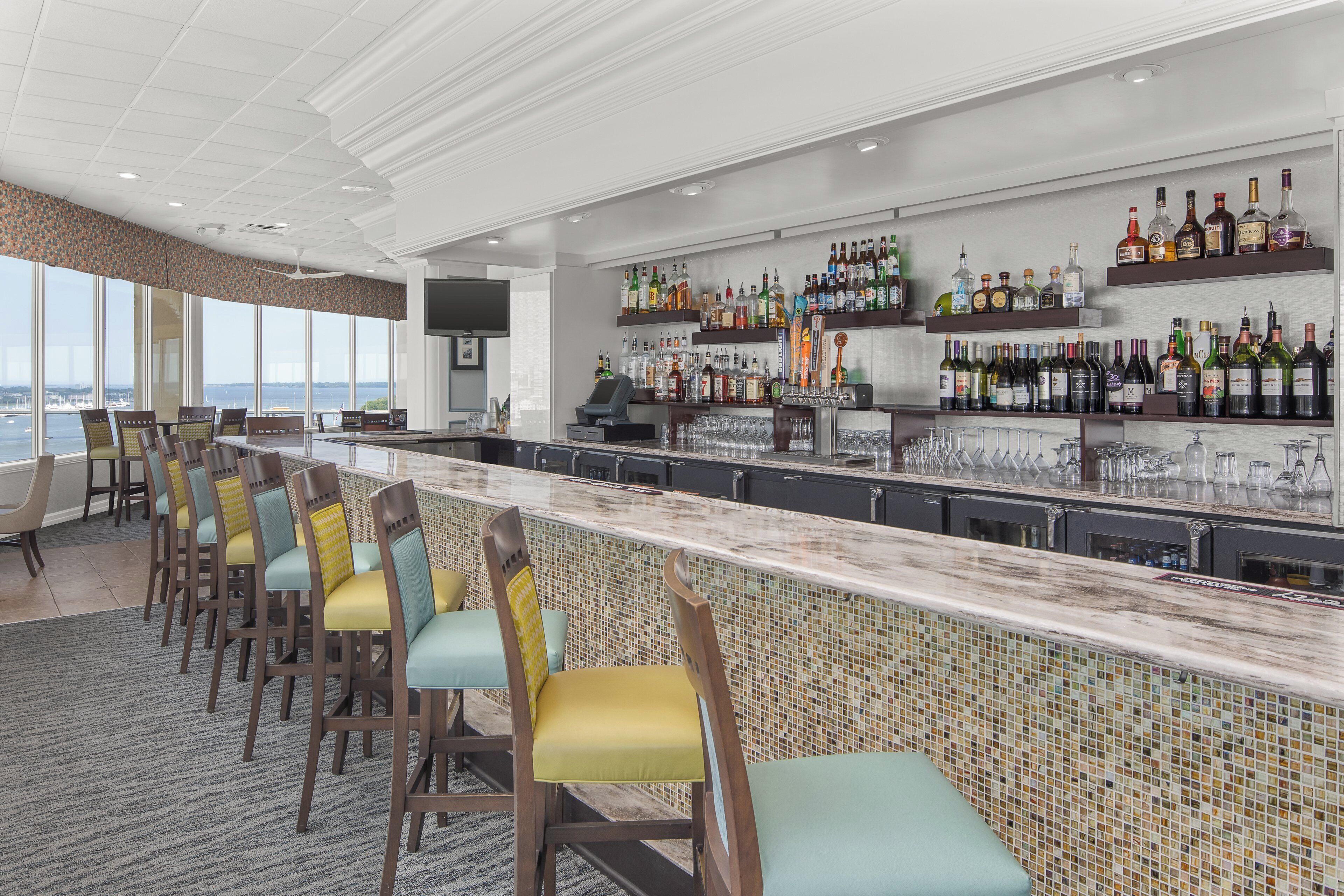 A bar area with a long counter, multiple seating options, and a variety of liquor bottles on shelves.