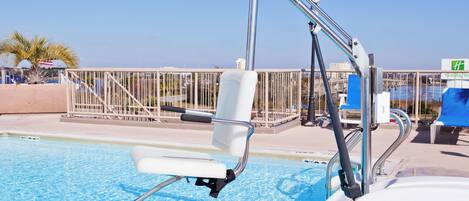 Zona de piscina con silla de salvavidas, sillas a la orilla y barandilla.