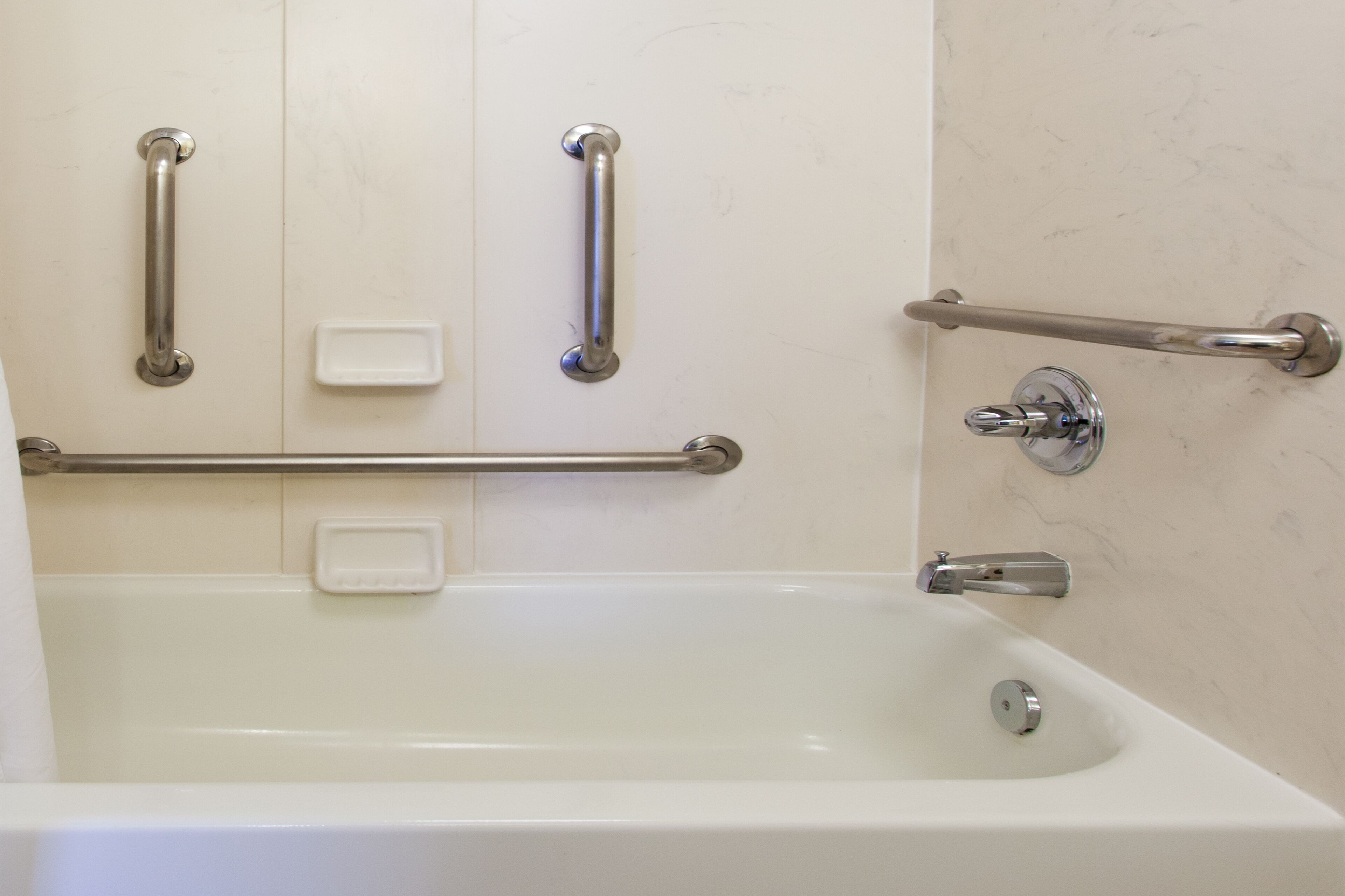 A bathroom with a white bathtub, grab bars, and a soap dish.