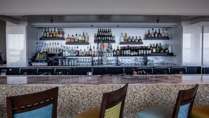 A bar area with multiple shelves of liquor bottles, a bar counter, and several chairs with cushioned seats. - Holiday Inn Charleston Riverview by IHG (Charleston)