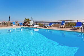 A clear blue pool with lounge chairs and a lifeguard stand.