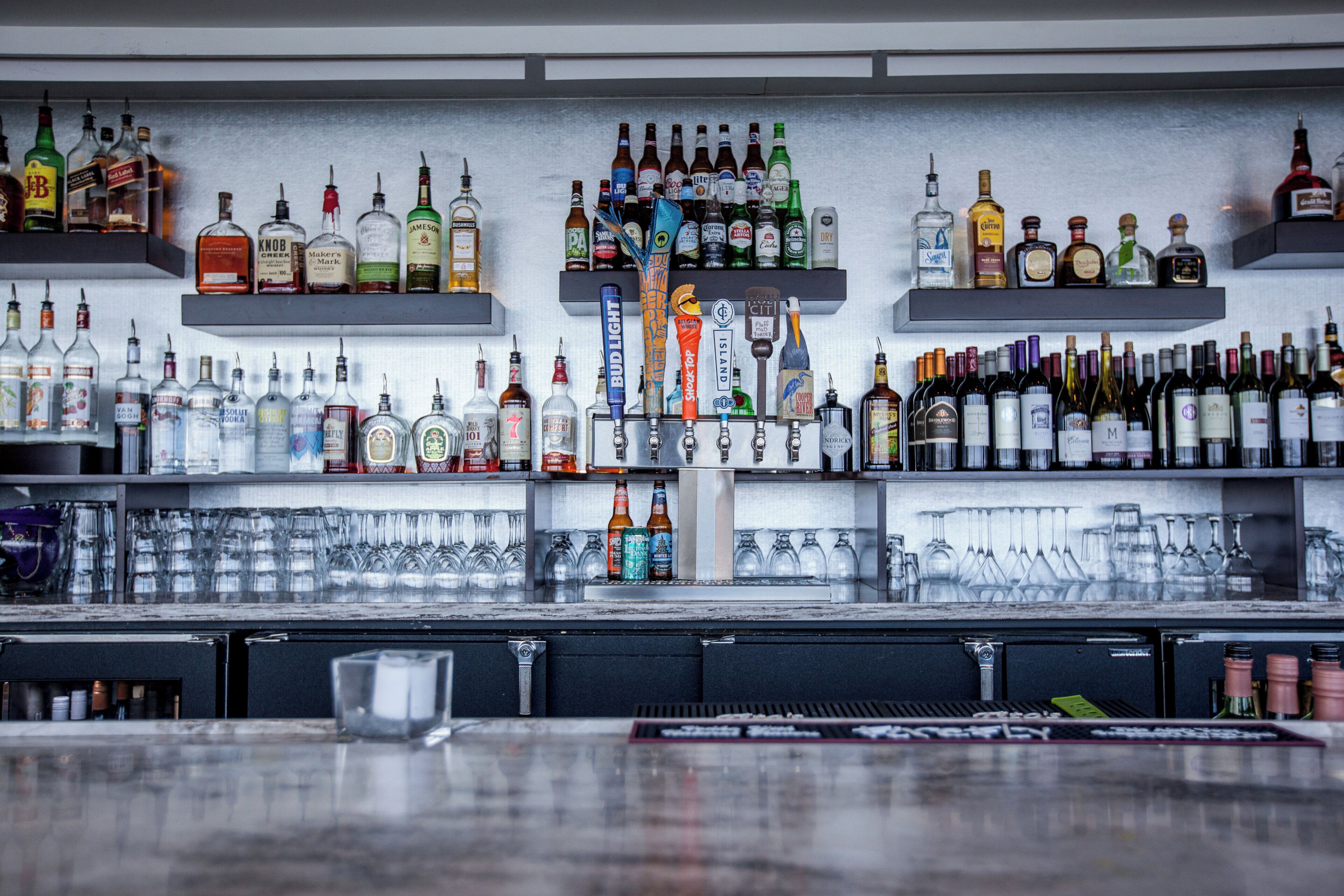 A bar with multiple shelves stocked with various bottles of alcohol and a selection of glasses.