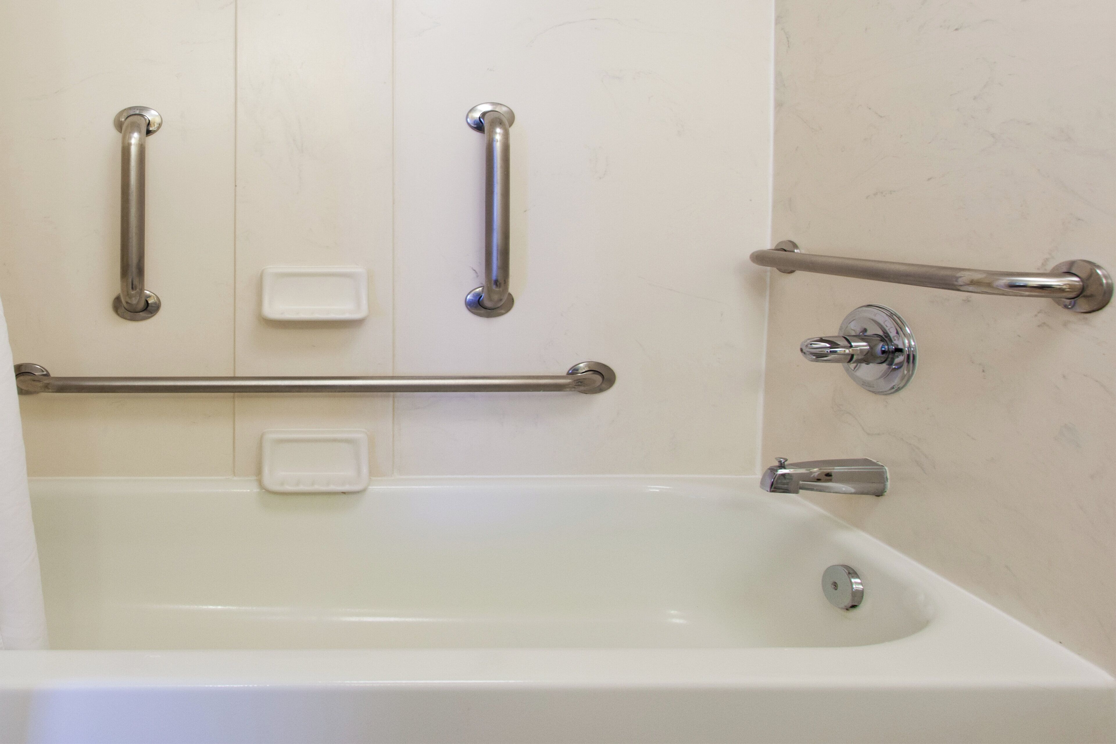 A bathroom with a bathtub, grab bars, and a soap dish.