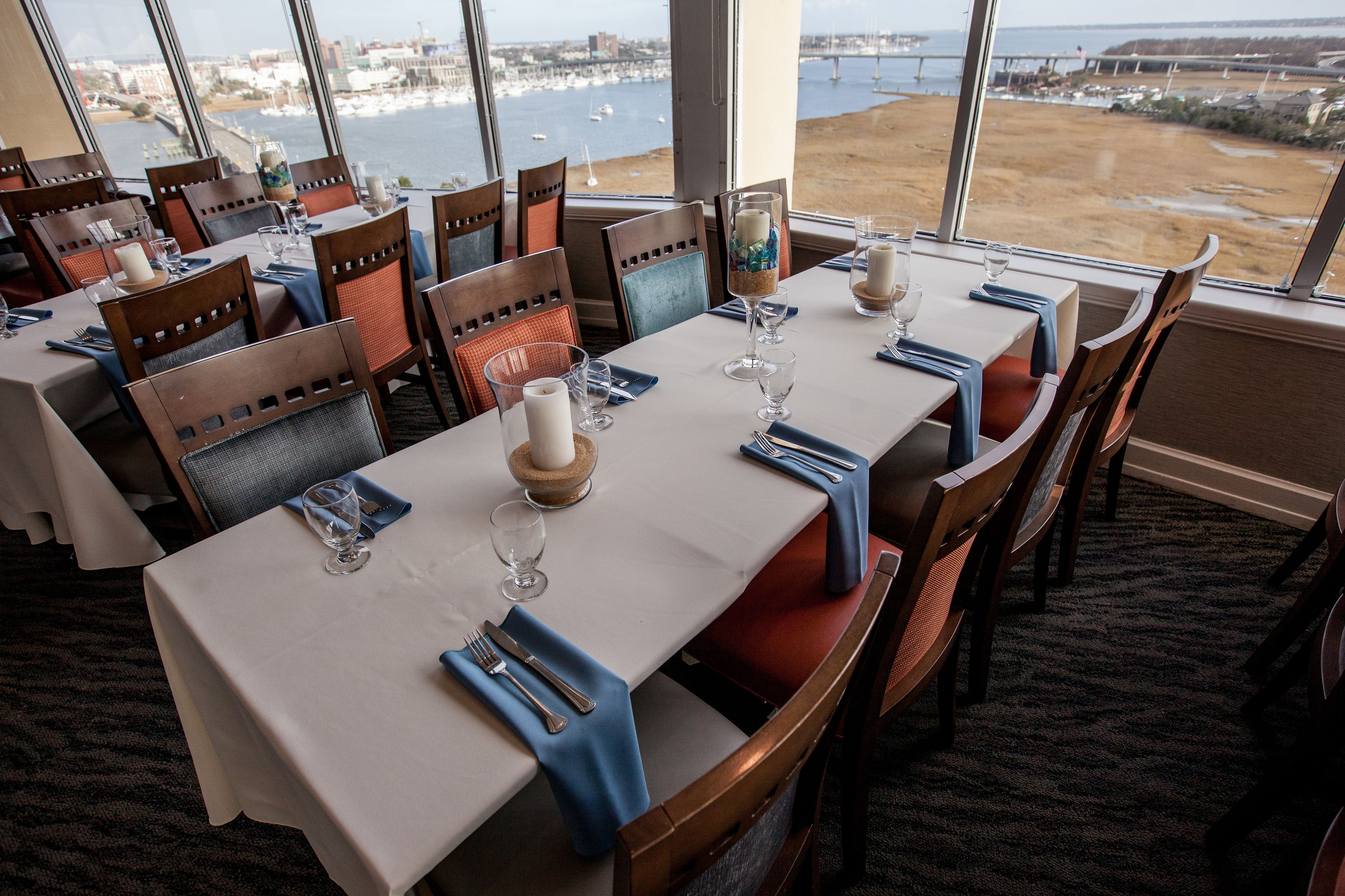 Un comedor con mesas dispuestas para cuatro, sillas con asientos acolchados y vistas al mar y a un puente.
