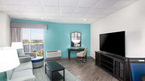 A modern hotel room with a large TV, comfortable seating, a desk, and a view of the city. - Holiday Inn Charleston Riverview by IHG (Charleston)