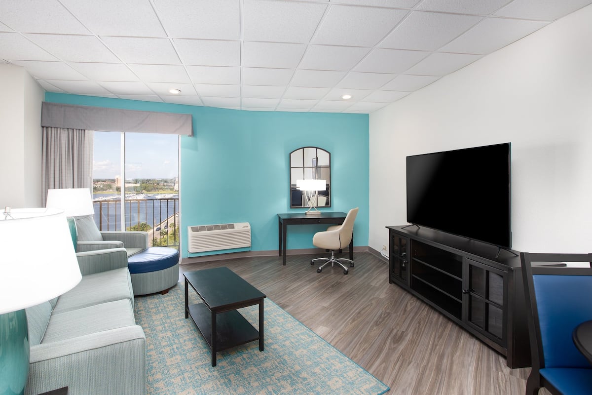 A modern hotel room with a large TV, comfortable seating, a desk, and a view of the city.