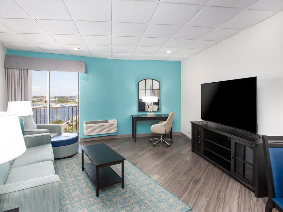A modern hotel room with a large TV, comfortable seating, a desk, and a view of the city.