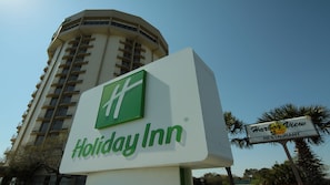A Holiday Inn sign with a green logo, a tall building in the background, and a sign for Harbor View Restaurant. - Holiday Inn Charleston Riverview by IHG (Charleston)