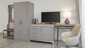A hotel room with a desk, a chair, a wardrobe, a television, and a lamp. - Holiday Inn Charleston Riverview by IHG (Charleston)