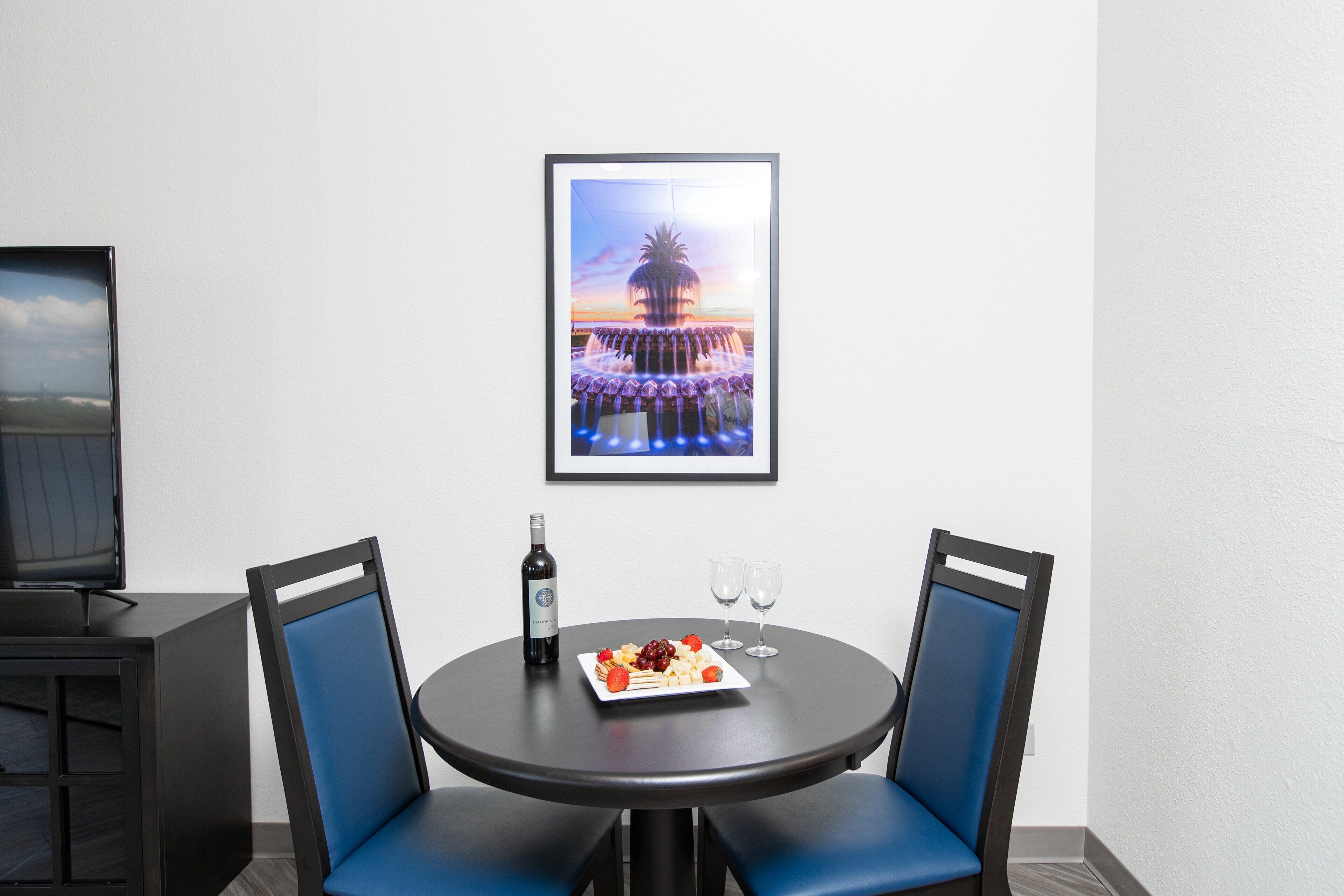 A dining area with a round table, two blue chairs, a bottle of wine, two glasses, and a plate of food.