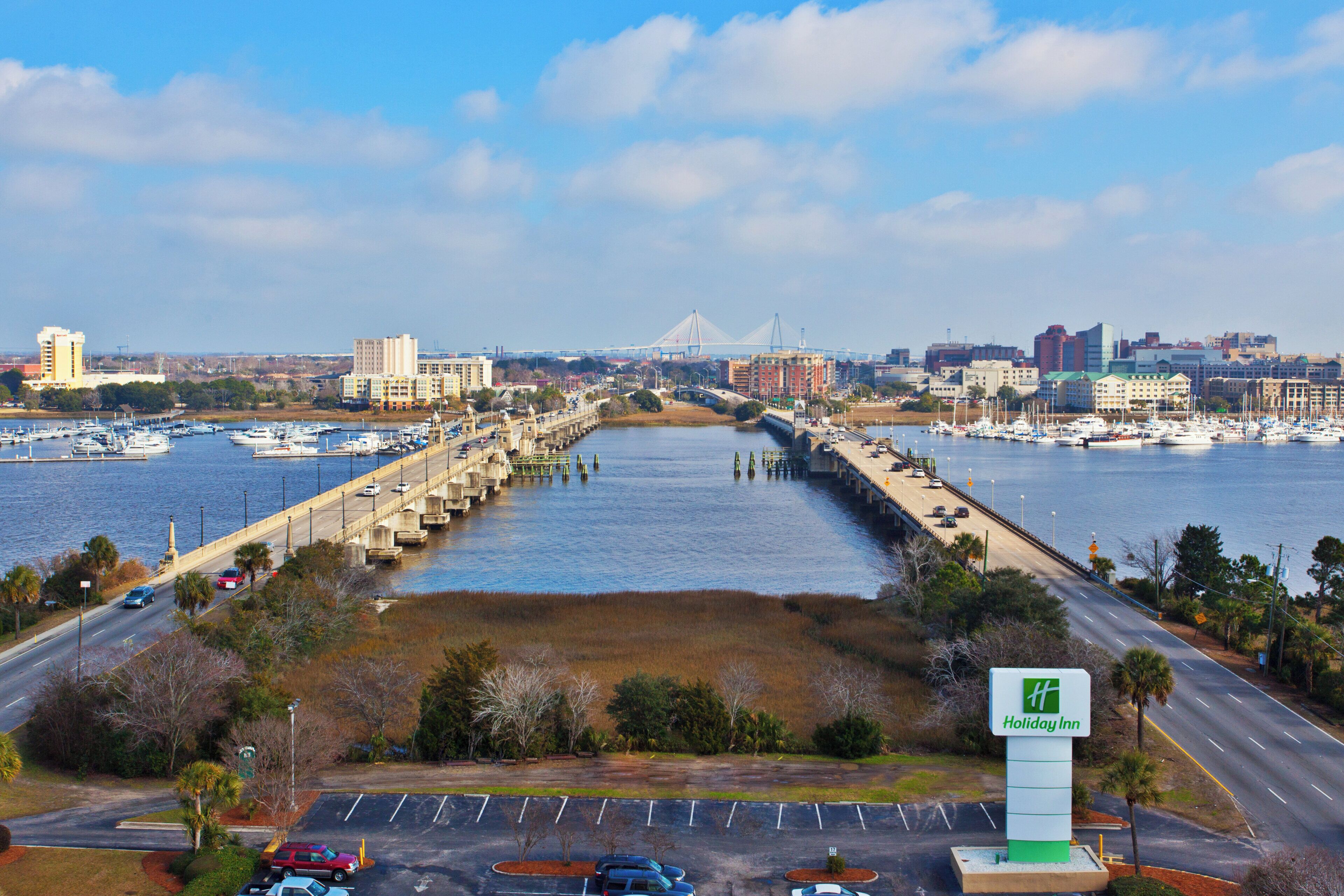 A Holiday Inn sign, a marina with boats, a bridge, and a city skyline in the background.
