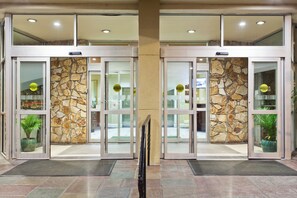 A hotel entrance with automatic doors, stone walls, and potted plants.