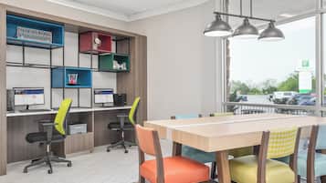 A modern office space with a long table, colorful chairs, and a desk with two monitors.