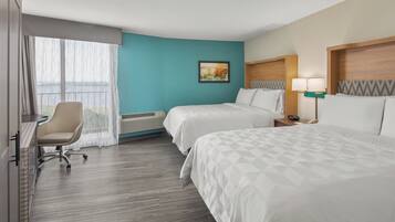 A hotel room with two beds, a desk, a chair, and a view of the outdoors.