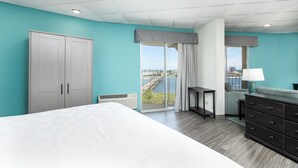 A modern hotel room with a large bed, a wardrobe, a desk, and a view of a cityscape through the window. - Holiday Inn Charleston Riverview by IHG (Charleston)