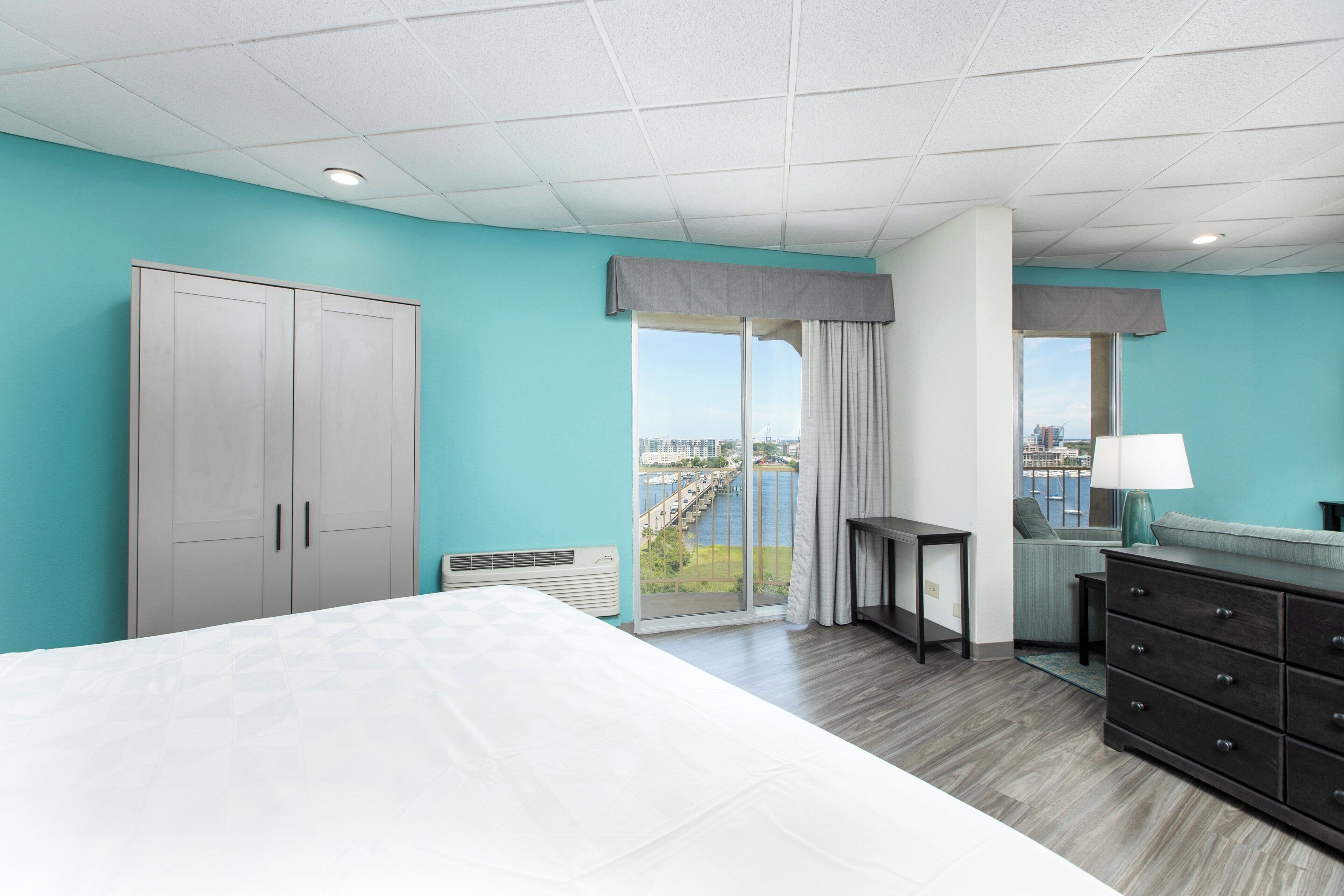 Une chambre d’hôtel avec un lit, une commode, une fenêtre donnant sur un beau paysage et un plafond doté d’un éclairage encastré.