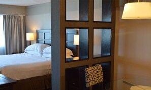 A hotel room with a bed, two bedside lamps, a mirror, and a chair with a patterned cushion. - Hilton Winnipeg Airport Suites (Winnipeg)