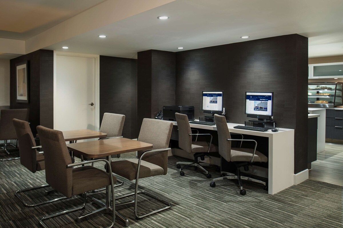 Un espacio de oficina moderno con una mesa de conferencias, sillas y dos puestos de trabajo con computadoras.
