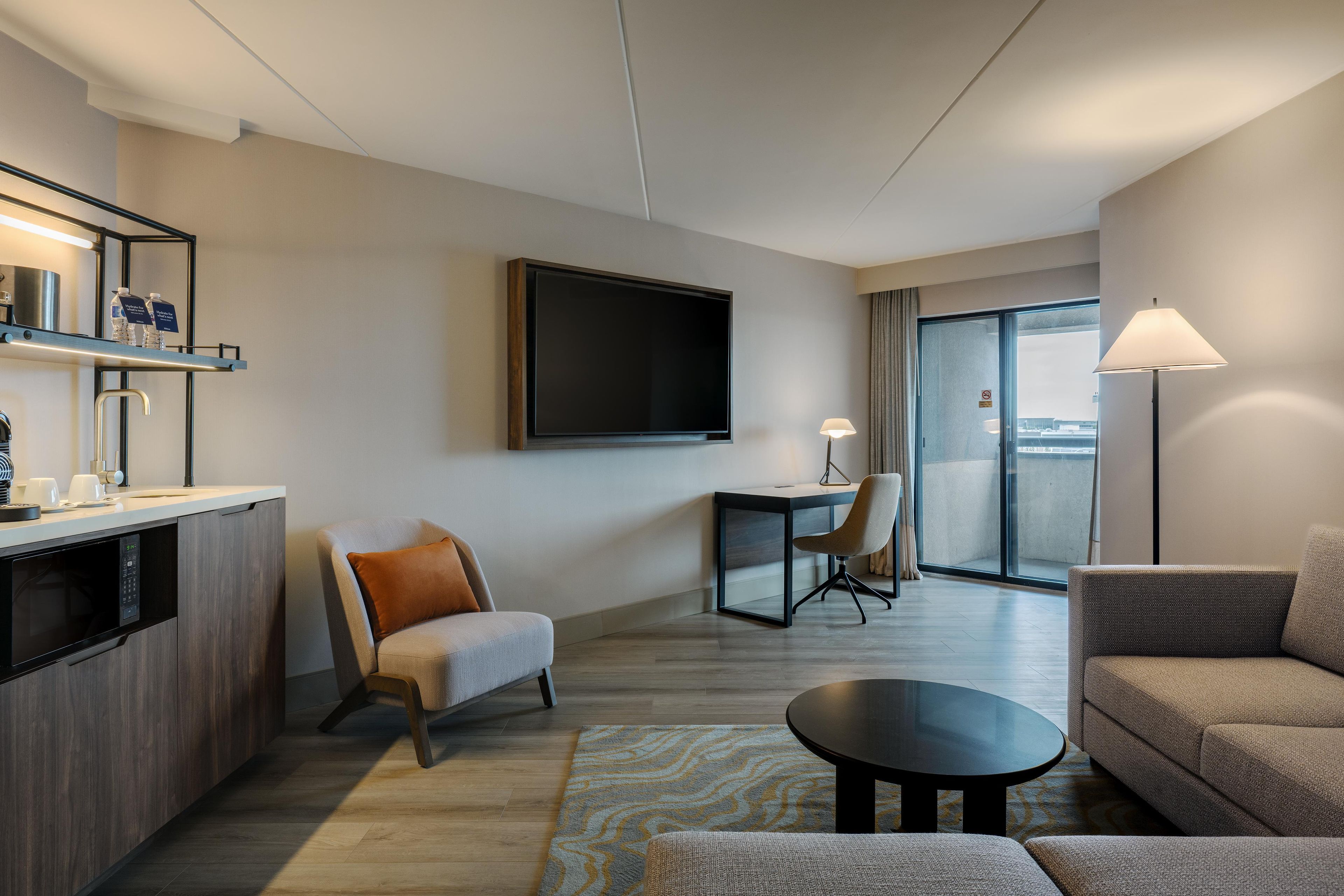 Une chambre d’hôtel moderne équipée d’une télévision à écran plat, d’un coin repas, d’un canapé, d’une table basse et d’un coin cuisine avec un four à micro-ondes.