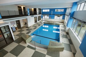 A large indoor swimming pool with checkered flooring, a balcony, and a view of the outdoors.