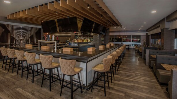 A modern bar area with a long counter, multiple stools, and a bar stocked with bottles.