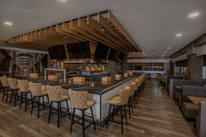 Eine moderne Bar mit einer langen Theke, mehreren Hockstühlen und einer Flaschenauswahl.