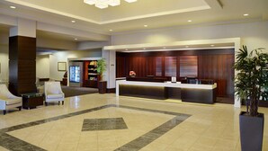 A modern lobby with a reception desk, seating area, and a large potted plant.