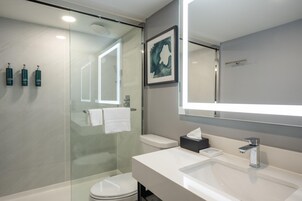 Un baño moderno con cabina de ducha de vidrio, inodoro blanco, lavabo con espejo y una obra de arte enmarcada en la pared.