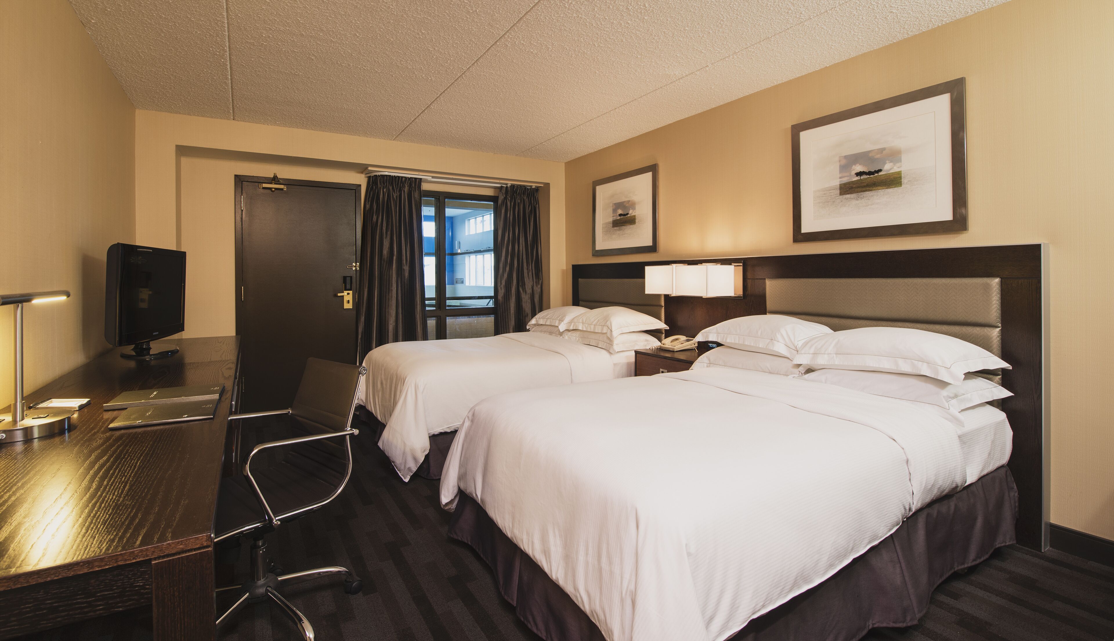 Une chambre d’hôtel avec deux lits, un bureau avec un ordinateur, un téléphone et une télévision.