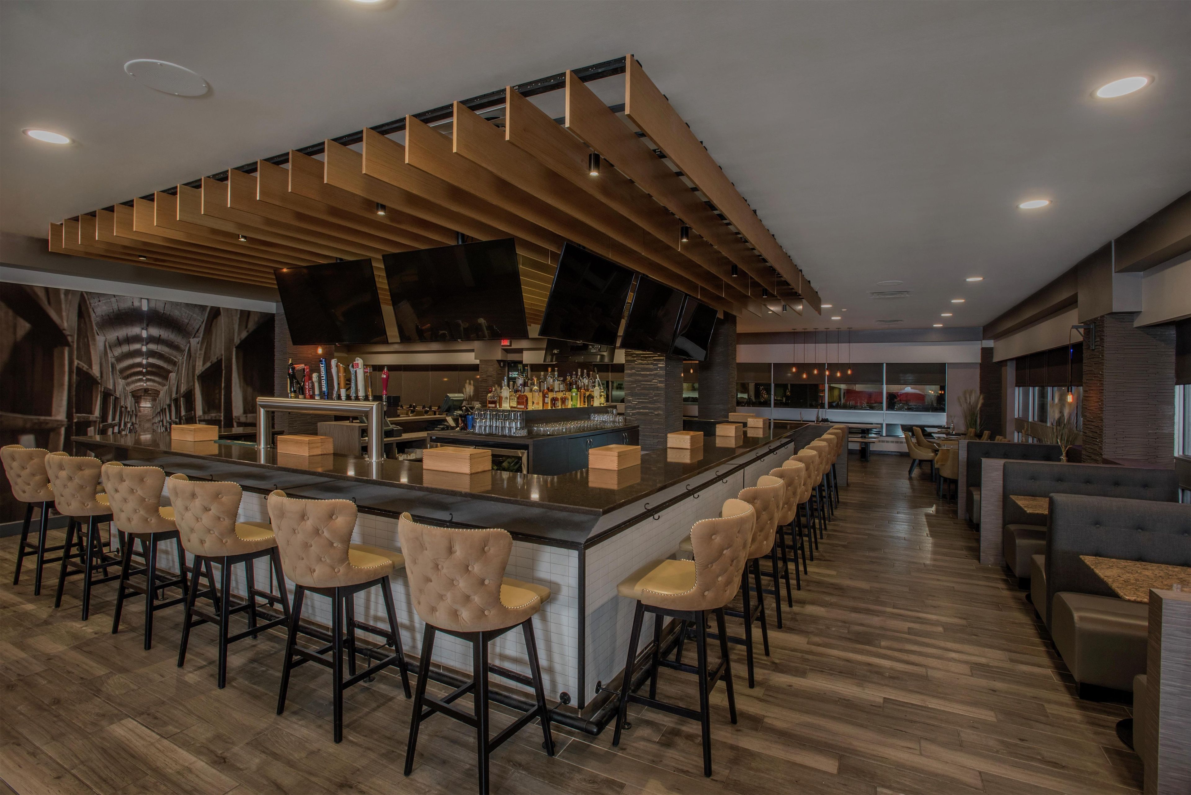 A bar area with a long counter, multiple stools, and a television screen.