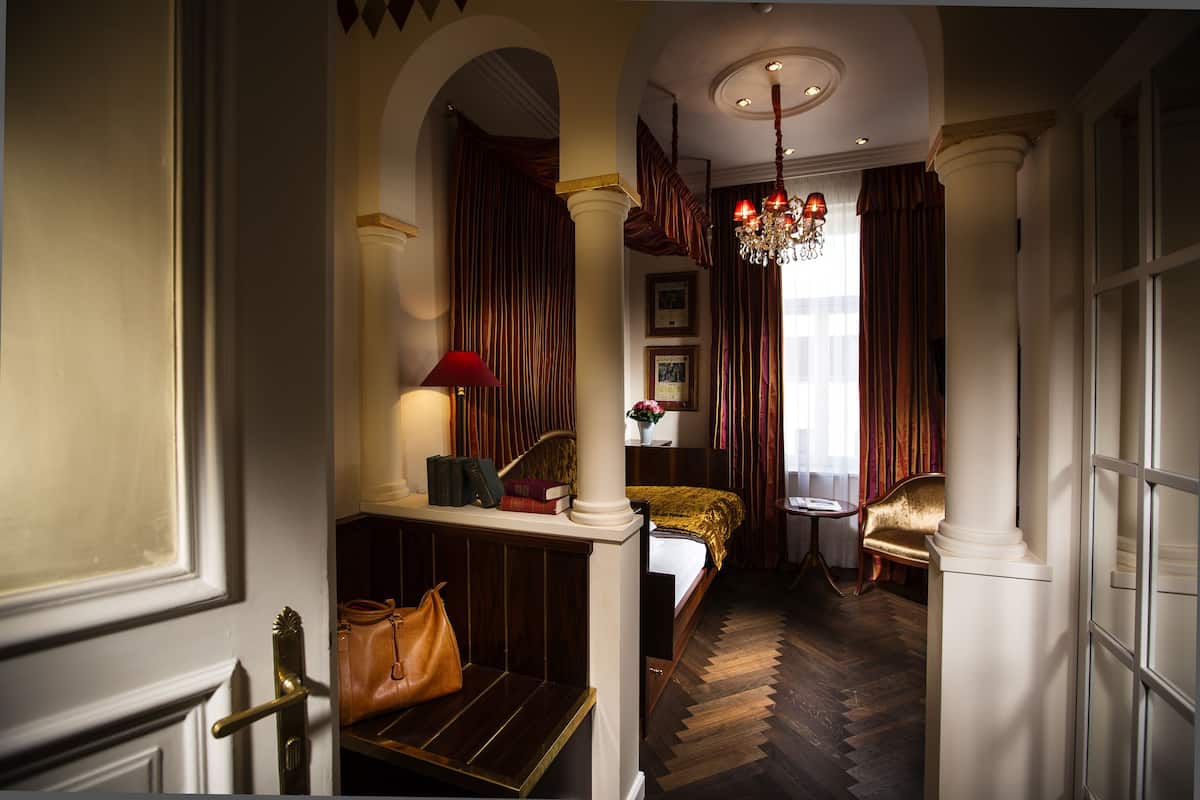 Ein Hotelzimmer mit Bett, einer Bank, einem Sessel, einer Chandelüster und Blick auf die Stadt.
