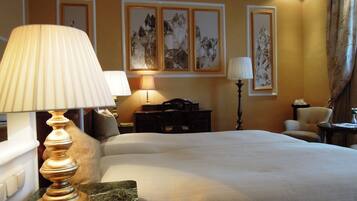 A hotel room with a bed, two bedside lamps, a desk, a chair, and artwork on the walls.