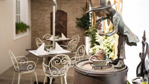 Un espacio al aire libre rústico con sillas y mesas de metal, una pared de ladrillo y una escultura decorativa de metal.