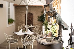 Un espacio al aire libre rústico con sillas y mesas de metal, una pared de ladrillo y una escultura decorativa de metal.