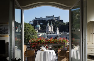 A dining area with a table set for two, overlooking a historic castle and lush greenery.