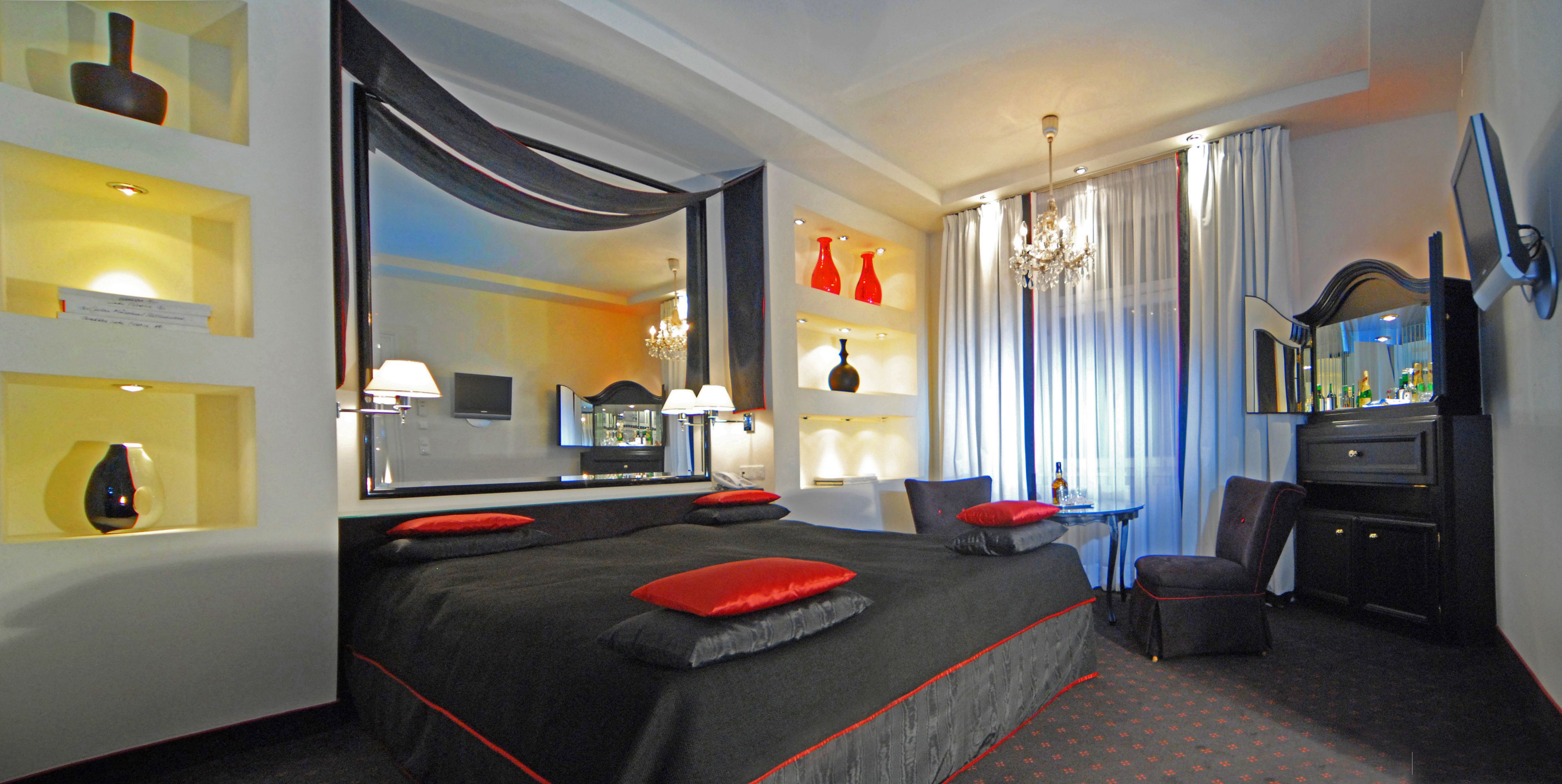 Ein Hotelzimmer mit einem großen Bett, einem Schreibtisch, einem Sessel, einem Spiegel und einer Chandelüster.